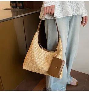 Detail view of a woven straw hobo bag with brown leather trim and small pouch hanging