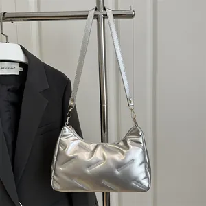 Borsa hobo trapuntata argento con finitura metallizzata appesa davanti a un blazer nero chic