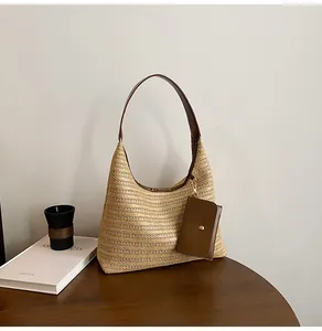 Detailed straw tote bag with brown leather strap and side-mounted square pouch on a wooden table