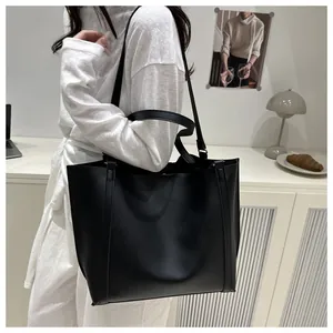 Minimalist large black PU leather tote bag shown in a cozy indoor lifestyle setting