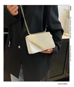 Detail of cream-white crossbody bag with woven texture and gold chain on black blazer