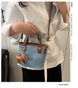 Detail einer blauen Denim-Beuteltasche mit braunem Lederbesatz und Hundeanhänger