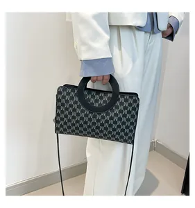 Detail of grey monogram square handbag featuring unique black circular handle and shoulder strap