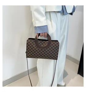 Detail view of the circular wooden handle and premium M-letter print on the crossbody bag