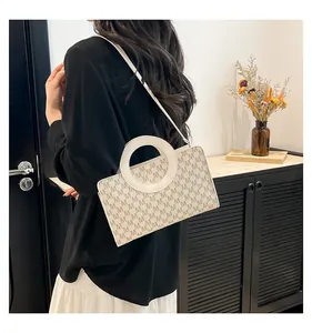 Detail of minimalist rectangular bag with monogram pattern and circular metal handle