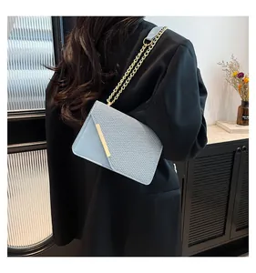 Detail of light blue woven crossbody bag with gold metal edge and chain strap on a model
