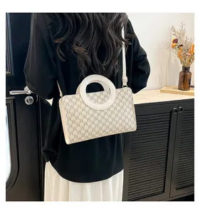 Detail of light beige crossbody bag with M-letter pattern and white circular handle