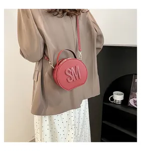 Detail of burgundy round leather crossbody bag featuring embossed SM logo on front