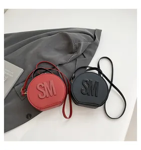 Close-up of circular crossbody bags in red and black with embossed letters and zippers