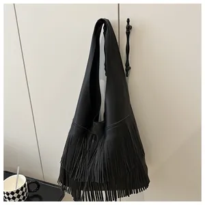 Detail of black lychee grain leather hobo bag with long fringe tassels on white cabinet
