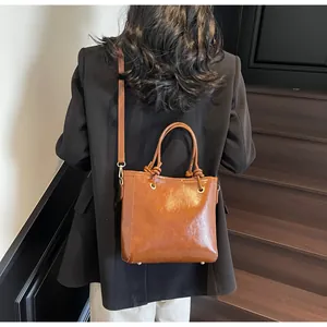 Sac seau en cuir marron porté en bandoulière sur fond d'escalier en bois