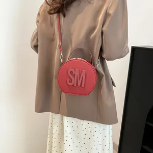 Chic red circular crossbody bag with SM embossed letters worn with a stylish brown suit