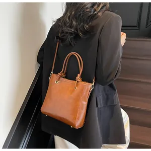 Détail du sac seau en cuir PU marron caramel avec poignée nouée sur un blazer noir