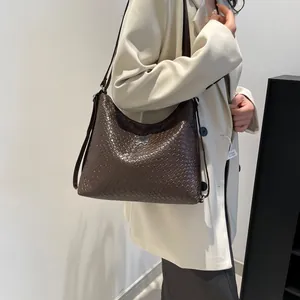 Sac hobo en cuir tressé marron foncé avec boucle nœud argenté porté avec un blazer beige