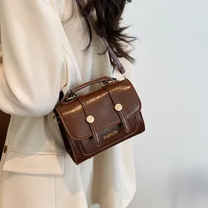Vintage dark brown crossbody bag with gold hardware worn by model in white blazer