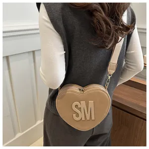 Detail of khaki heart-shaped crossbody bag featuring embossed SM lettering on a model