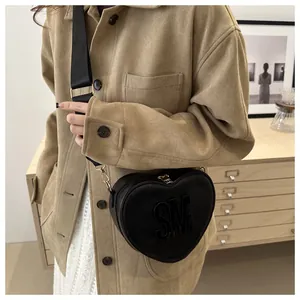 Detail of heart-shaped black leather crossbody bag featuring 3D SM logo worn by model