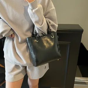 Sac seau classique en cuir noir avec détails dorés porté par un mannequin en gris