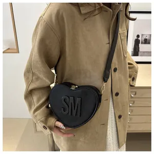 Close-up of heart-shaped black leather bag with embossed SM logo and gold zipper detail