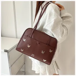 Détail d'un sac à épaule en cuir marron avec des papillons métalliques et doubles anses