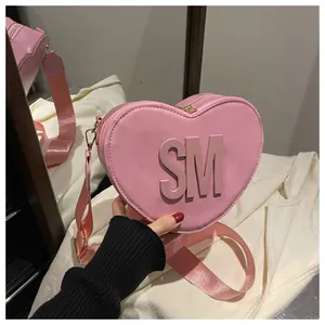 Detail view of pink heart-shaped bag with bold SM metal logo and wide textile strap