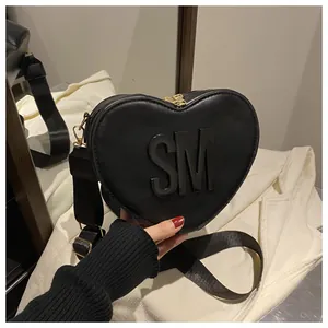 Detail of heart-shaped black crossbody bag with embossed SM letters and gold zippers