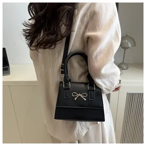 Detail of black crossbody bag with gold bow clasp worn by model in minimalist setting