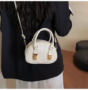 Model met een crème PU-leren handtas met gouden gespen en een slanke, verstelbare schouderriem