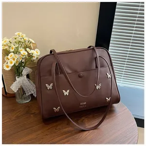 Détail d'un sac cabas marron foncé avec ornements papillon argentés sur une table