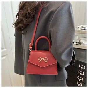 Close-up of red trapezoid handbag with gold bow ornament and matte leather texture