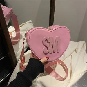 Pink heart-shaped crossbody bag with embossed letters and adjustable wide fabric strap
