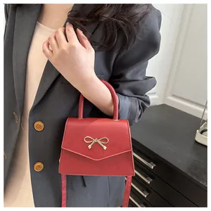 Close-up of red structured handbag featuring a gold bow accent on a grey blazer outfit
