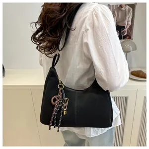 Vista de cerca del bolso hobo negro con colgantes de cuerda y accesorios metálicos