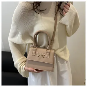 Detail of beige crossbody bag featuring a golden bow ornament and smooth faux leather
