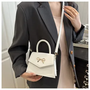 White mini crossbody bag with gold bow clasp on grey suit showing scale and fit
