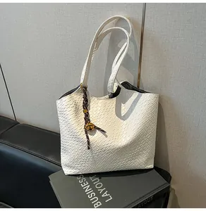 Détail du sac cabas blanc à texture tissée, anses longues et pendentif métallique