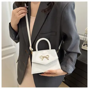 Close-up of white mini handbag with golden bow metal buckle and matte leather texture