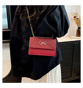 Close-up of wine red handbag featuring a gold bow buckle and textured leather flap