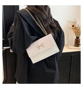 Detail of cream crossbody bag with gold bow buckle and crocodile texture on model