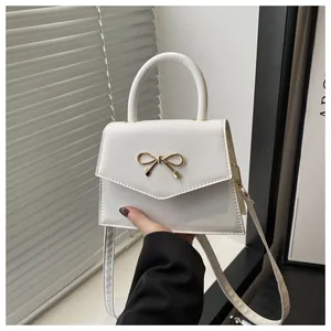 Close-up of a white leather crossbody bag featuring a golden metal bow decoration