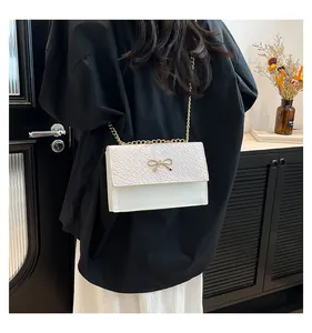 Close-up of white embossed bow handbag with gold chain strap worn by a model