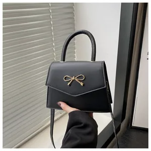 Detail of a black square handbag with a golden bow buckle and smooth matte leather texture