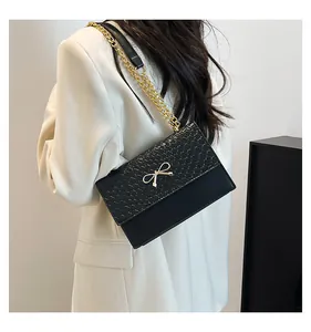 Detail of black bow shoulder bag with snake skin texture and gold chain worn with white blazer