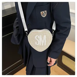Detail of heart-shaped woven crossbody bag featuring SM embroidery and white strap
