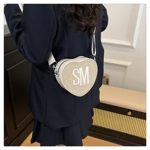 Detailed view of heart-shaped woven bag with SM embroidery on a model shoulder
