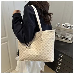 Close-up of a large tote bag with M-pattern logo and metallic circular charm detail