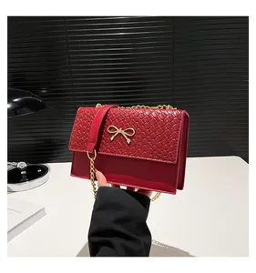 Close-up of red handbag featuring a gold bow buckle and elegant metal chain strap