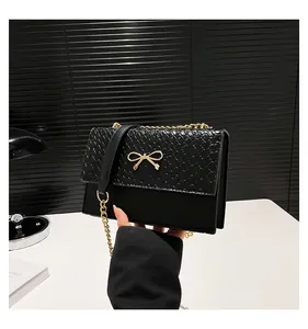 Detail of black crossbody bag featuring a golden bow buckle and woven leather texture