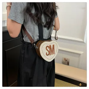 Detail of heart-shaped woven crossbody bag with leather trim and SM embroidery