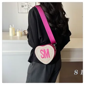 Detail shot of heart-shaped woven bag with pink SM letter embroidery and wide strap